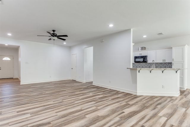 unfurnished living room featuring light hardwood / wood-style floors, ceiling fan, and sink