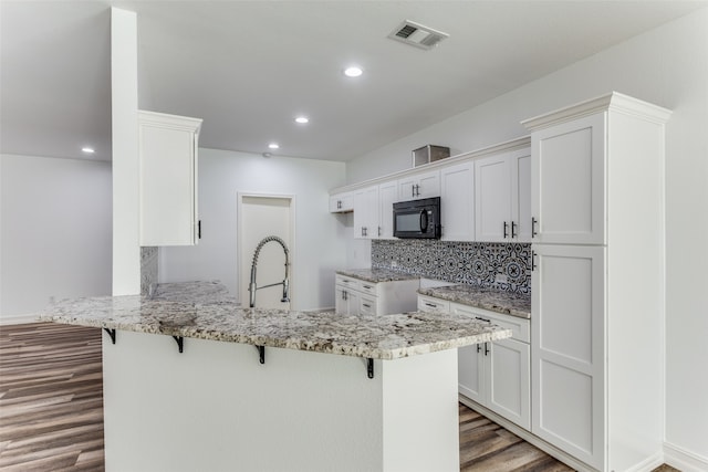 kitchen with dark wood-type flooring, backsplash, kitchen peninsula, a kitchen bar, and white cabinets