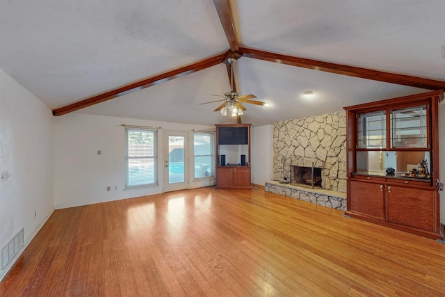 unfurnished living room featuring lofted ceiling with beams, light hardwood / wood-style floors, a fireplace, and ceiling fan