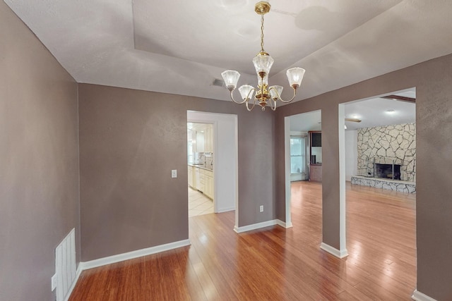 unfurnished dining area featuring hardwood / wood-style floors, a stone fireplace, and a notable chandelier