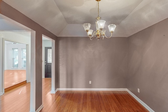 unfurnished dining area with lofted ceiling, a notable chandelier, and hardwood / wood-style flooring