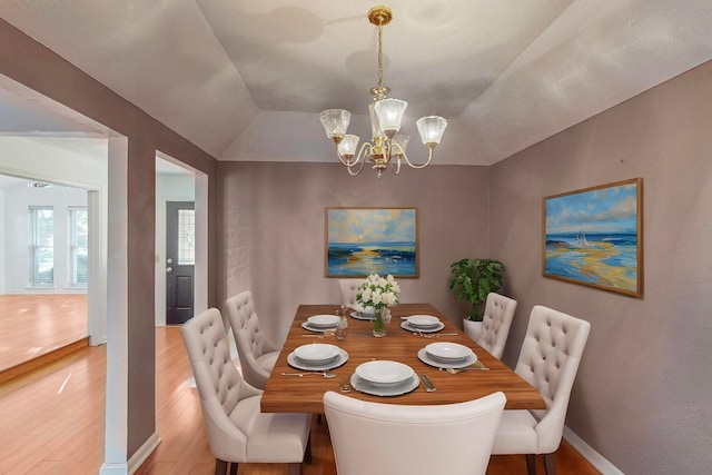 dining area featuring wood-type flooring, vaulted ceiling, and an inviting chandelier