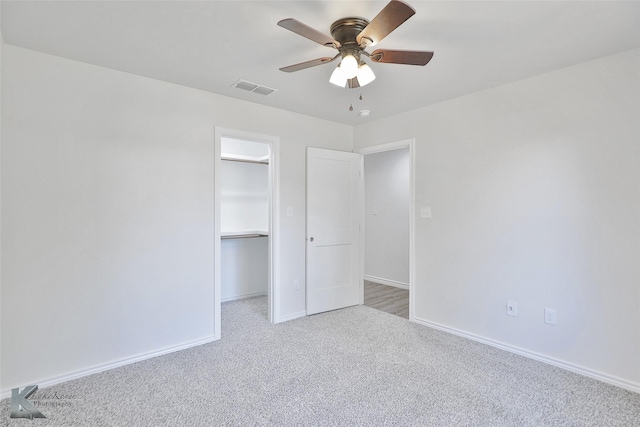 unfurnished bedroom featuring light carpet, a closet, a spacious closet, and ceiling fan