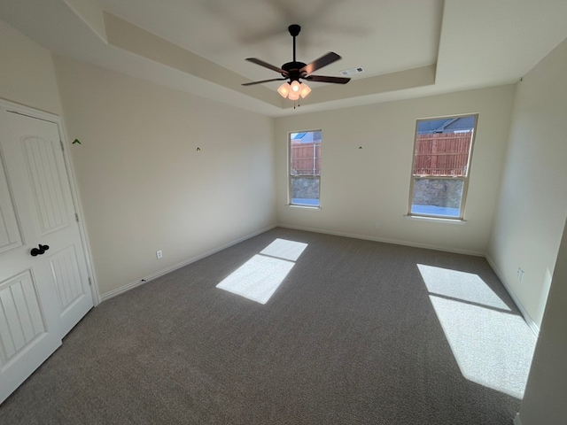 spare room featuring dark colored carpet, a raised ceiling, and ceiling fan