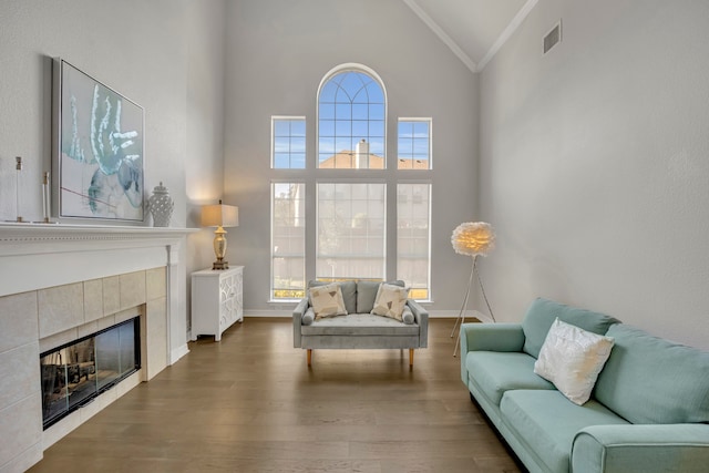 living room with a tiled fireplace, crown molding, high vaulted ceiling, and dark hardwood / wood-style floors