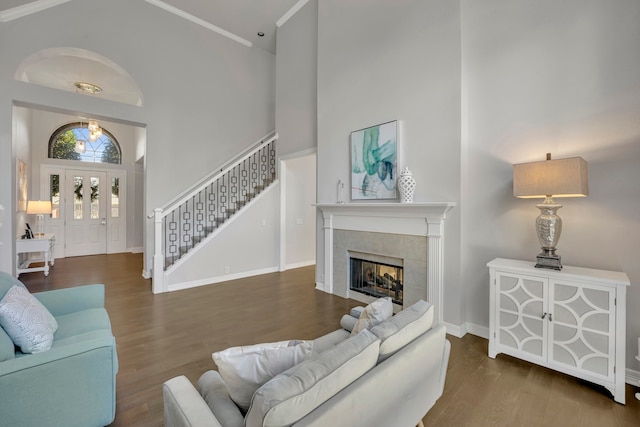 living room featuring wood-type flooring, a fireplace, a towering ceiling, and ornamental molding