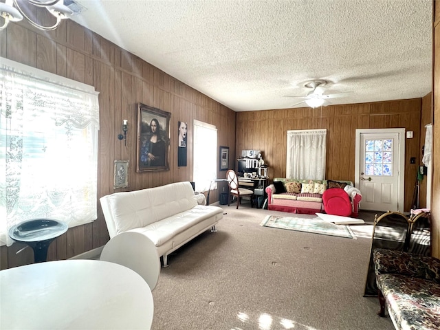 carpeted living room with a ceiling fan, wood walls, and a textured ceiling