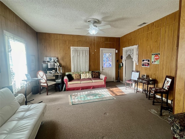 carpeted living room with wooden walls, visible vents, ceiling fan, and a textured ceiling