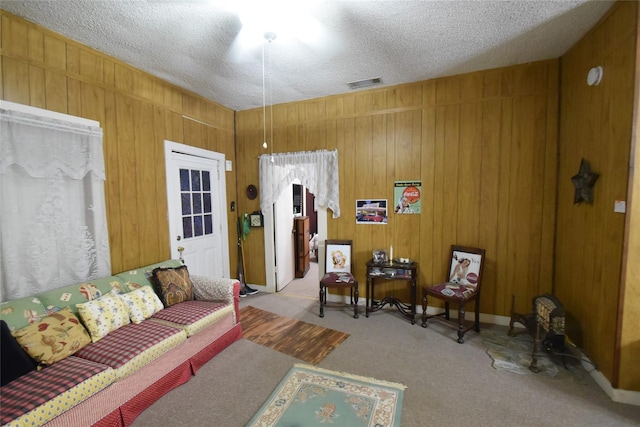 carpeted living room with wood walls, visible vents, and a textured ceiling