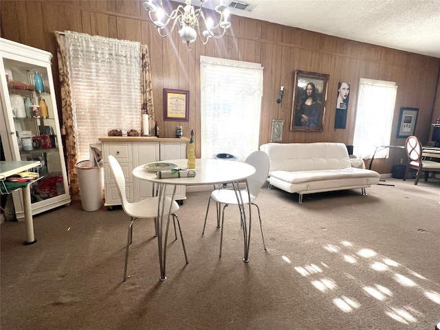 carpeted dining room featuring a textured ceiling, wood walls, visible vents, and a notable chandelier