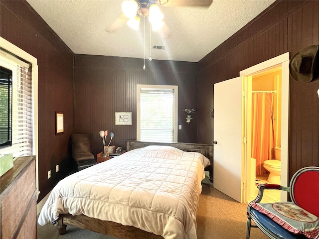 carpeted bedroom featuring a textured ceiling, a ceiling fan, visible vents, and wooden walls