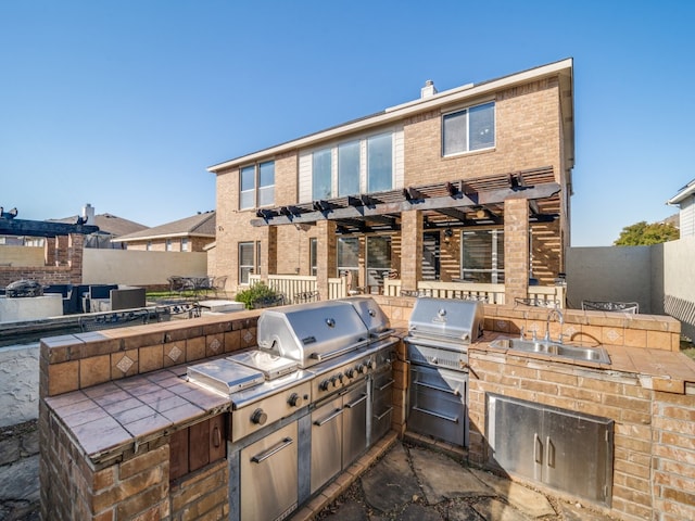 view of patio with an outdoor kitchen, area for grilling, a pergola, and sink