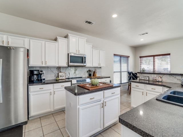 kitchen with light tile patterned floors, a kitchen island, tasteful backsplash, white cabinets, and appliances with stainless steel finishes