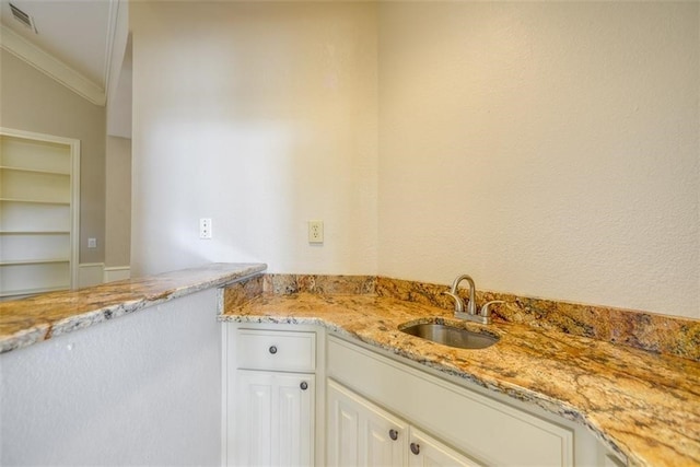 kitchen with light stone countertops, ornamental molding, sink, white cabinetry, and lofted ceiling