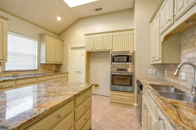 kitchen featuring tasteful backsplash, light stone counters, vaulted ceiling, sink, and cream cabinetry