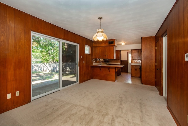 kitchen with kitchen peninsula, pendant lighting, light colored carpet, and wooden walls