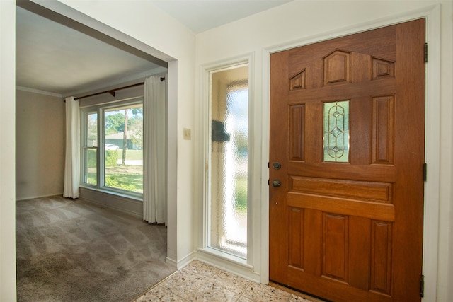 foyer entrance with ornamental molding and light carpet