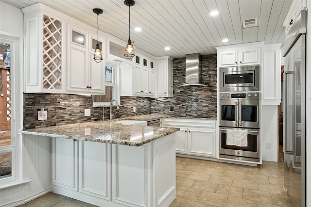 kitchen featuring kitchen peninsula, light stone counters, sink, wall chimney range hood, and white cabinetry