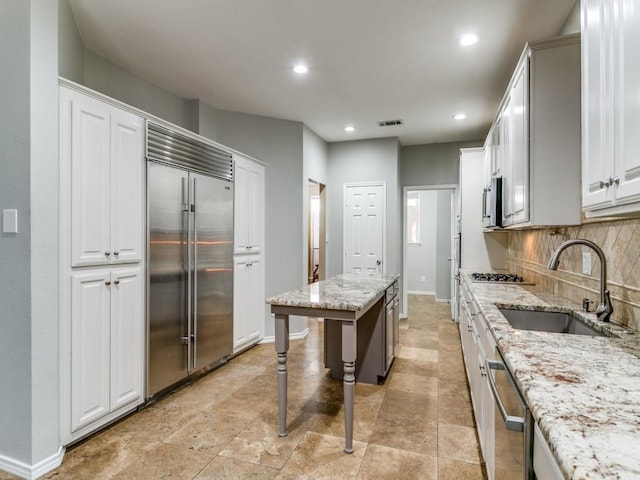 kitchen with sink, appliances with stainless steel finishes, backsplash, light stone counters, and white cabinets