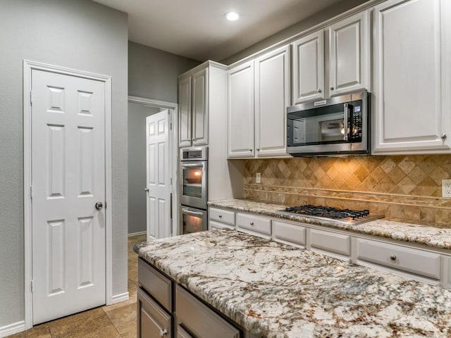 kitchen with appliances with stainless steel finishes, white cabinetry, decorative backsplash, light tile patterned floors, and light stone countertops