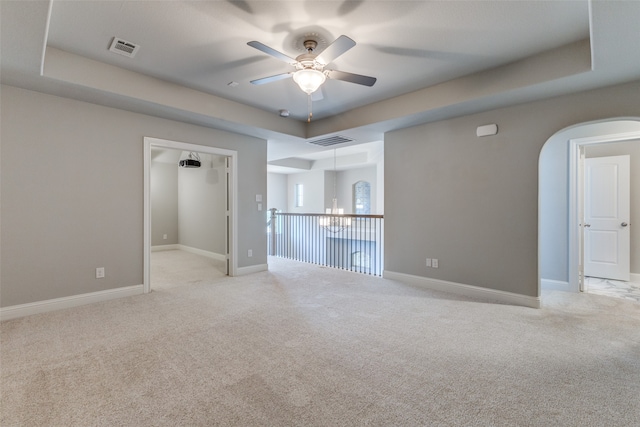 carpeted empty room with ceiling fan with notable chandelier and a tray ceiling