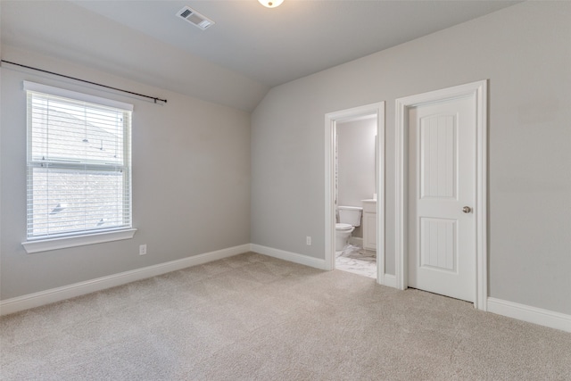 unfurnished bedroom with connected bathroom, light carpet, and vaulted ceiling