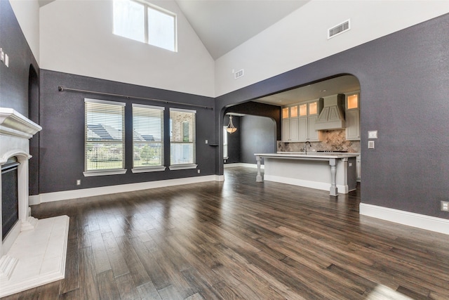 unfurnished living room featuring sink, dark hardwood / wood-style flooring, a fireplace, and high vaulted ceiling