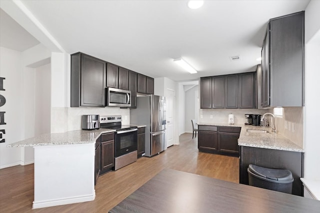 kitchen featuring sink, stainless steel appliances, light hardwood / wood-style flooring, backsplash, and dark brown cabinets