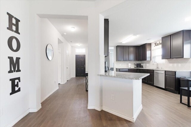 kitchen with dishwasher, light stone countertops, dark brown cabinets, light hardwood / wood-style floors, and kitchen peninsula