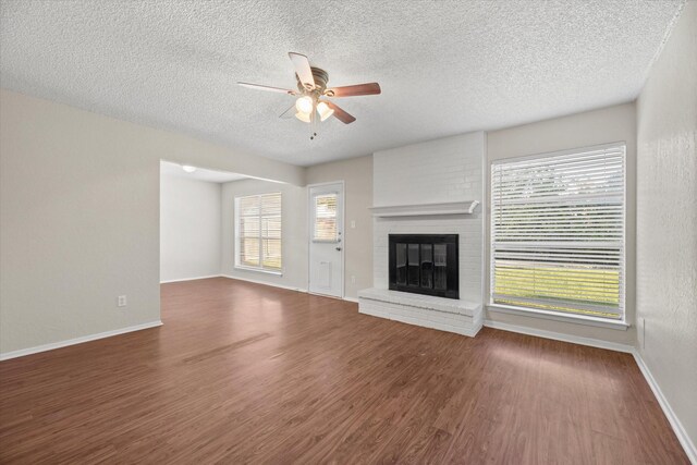 unfurnished living room with ceiling fan, dark hardwood / wood-style flooring, a textured ceiling, and a brick fireplace