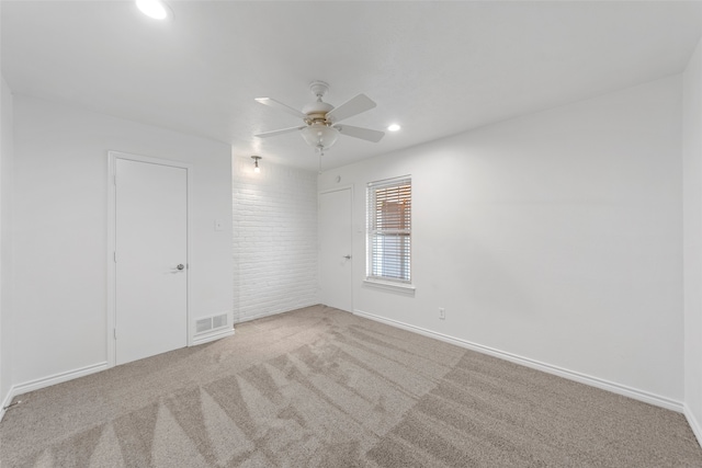 carpeted empty room featuring ceiling fan and brick wall