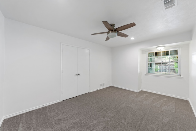 spare room featuring ceiling fan and dark carpet