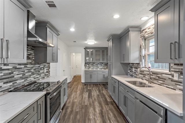 kitchen with dark wood-type flooring, wall chimney range hood, sink, decorative backsplash, and stainless steel appliances