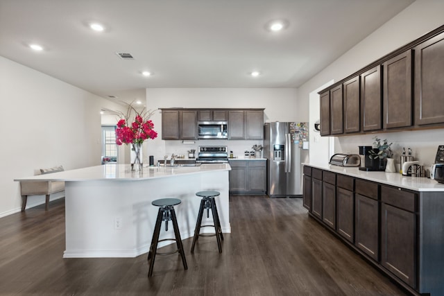 kitchen featuring dark wood-type flooring, dark brown cabinetry, stainless steel appliances, and a center island with sink