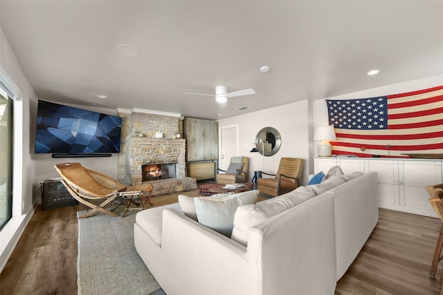 living room with a stone fireplace, ceiling fan, and dark wood-type flooring