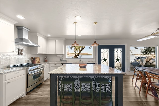 kitchen with dark hardwood / wood-style flooring, high end stainless steel range oven, wall chimney exhaust hood, and light stone counters