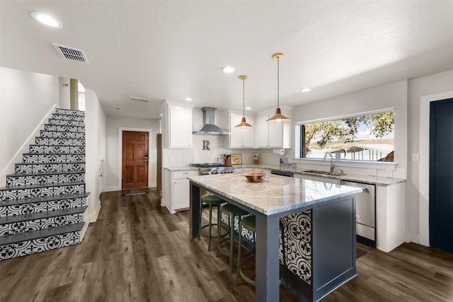 kitchen with white cabinets, wall chimney exhaust hood, a kitchen island, light stone counters, and stainless steel appliances