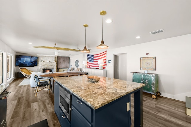 kitchen featuring dark wood-type flooring, blue cabinetry, decorative light fixtures, a stone fireplace, and stainless steel microwave