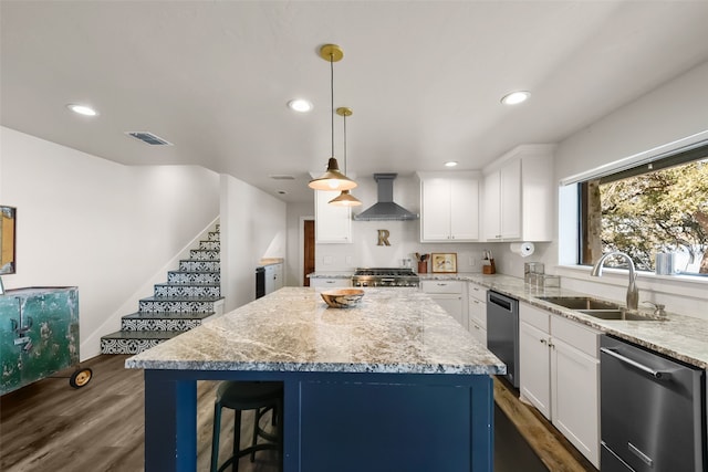 kitchen featuring pendant lighting, wall chimney range hood, sink, appliances with stainless steel finishes, and a kitchen island