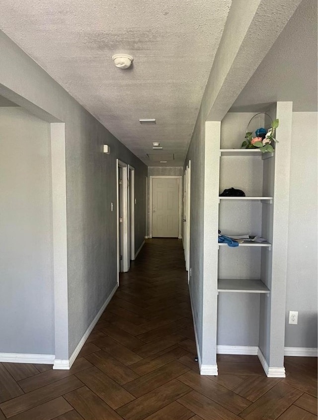 hall featuring dark parquet floors, built in features, and a textured ceiling