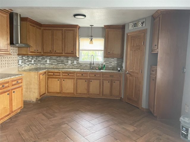 kitchen featuring backsplash, sink, hanging light fixtures, and wall chimney range hood