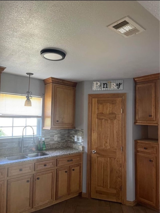 kitchen featuring a textured ceiling, tasteful backsplash, hanging light fixtures, and sink