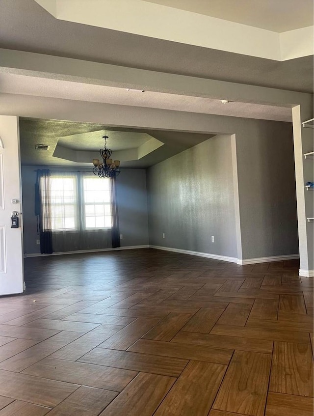 unfurnished room featuring dark parquet flooring, a raised ceiling, and a notable chandelier