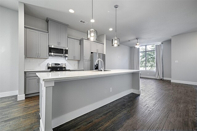 kitchen featuring sink, stainless steel appliances, pendant lighting, gray cabinets, and a center island with sink