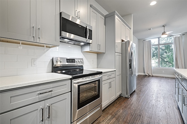 kitchen with decorative backsplash, appliances with stainless steel finishes, dark hardwood / wood-style flooring, light stone counters, and ceiling fan