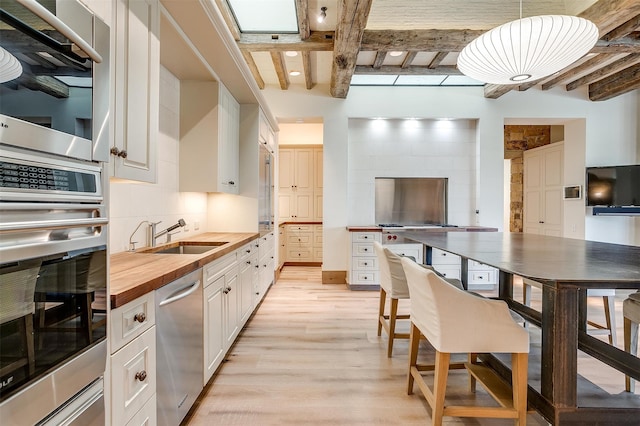 kitchen featuring wood counters, appliances with stainless steel finishes, sink, beam ceiling, and white cabinets