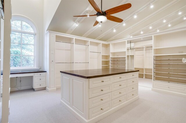 spacious closet with ceiling fan, light colored carpet, built in desk, and vaulted ceiling