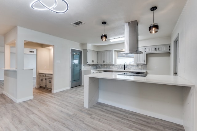 kitchen featuring hanging light fixtures, decorative backsplash, light wood-type flooring, kitchen peninsula, and island exhaust hood