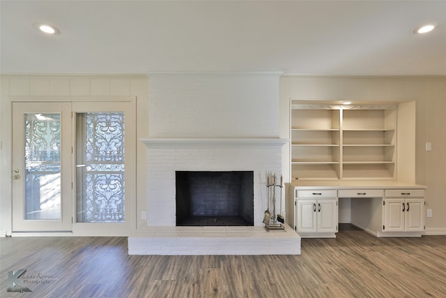 unfurnished living room featuring hardwood / wood-style flooring, built in desk, ornamental molding, and a brick fireplace