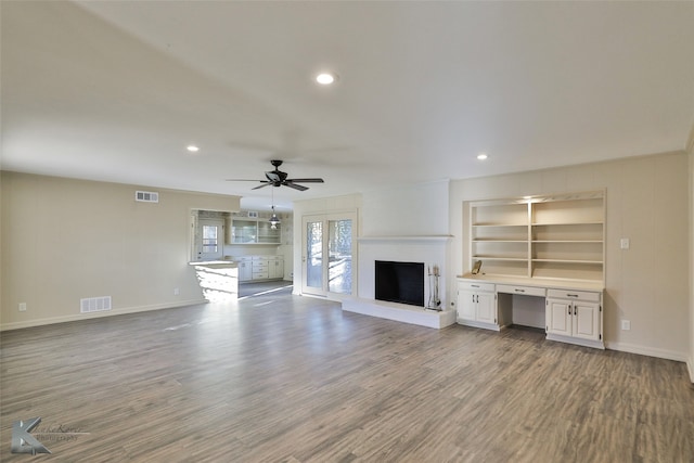 unfurnished living room with hardwood / wood-style flooring, ceiling fan, a large fireplace, and built in desk